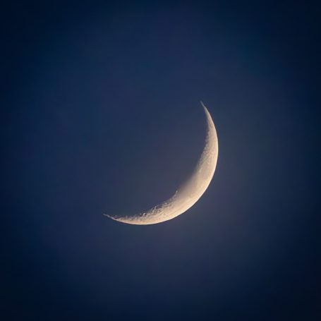 Zarte Sichel des Mondes vor einem tiefblauen Himmel.