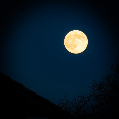 Helle Vollmond am nächtlichen Himmel, umgeben von dunklem Raum und Silhouetten.