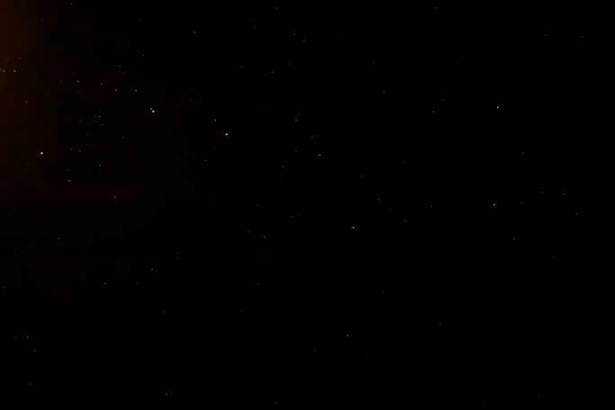 Dunkler Hintergrund mit schwachem Lichtpunkt und vereinzelten kleinen Lichtpunkten.