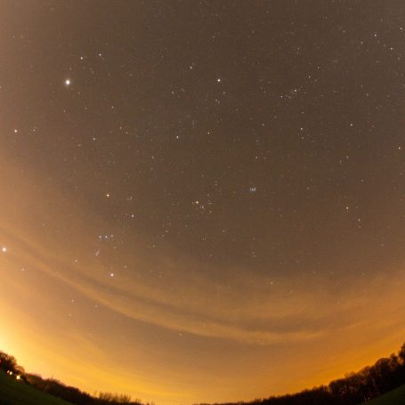 Sternenhimmel mit hellen Sternen und orangefarbenem Licht am Horizont.
